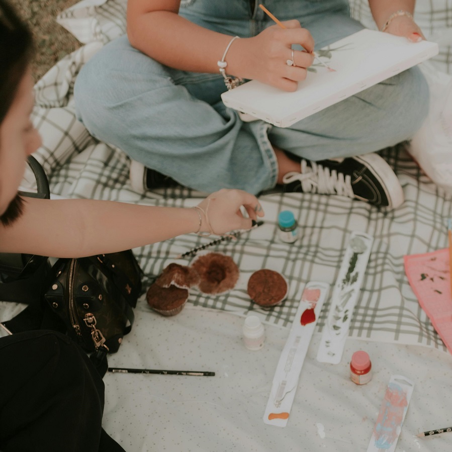 Two friends sitting on the grass and painting.